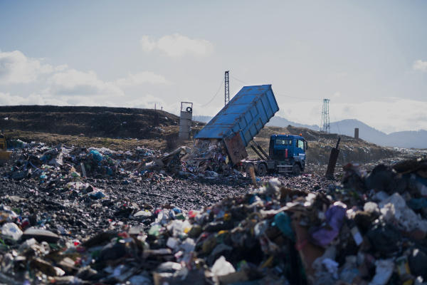 Garbage truck unloading waste on landfill, environmental concept. Copy space.