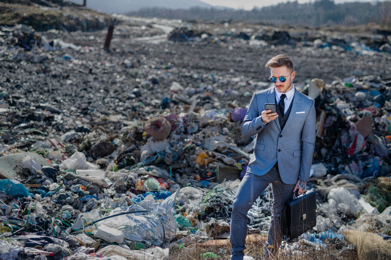 Fashionable modern businessman with smartphone on landfill, consumerism versus pollution concept.