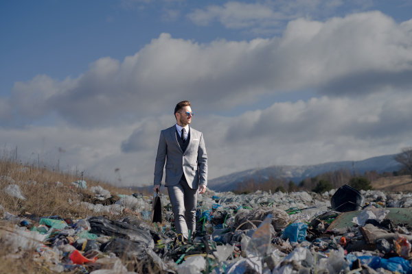 Fashionable modern businessman on landfill, consumerism versus pollution concept.