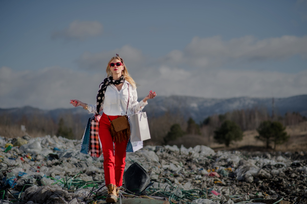 Fashionable modern woman with shopping bags on landfill, consumerism versus pollution concept.