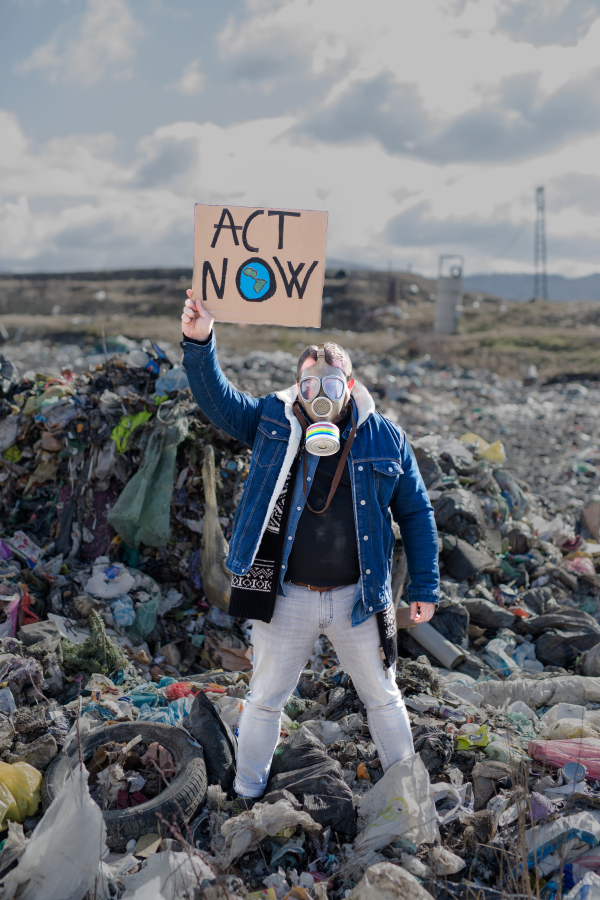 Front view of man with gas mask and placard poster on landfill, environmental concept.