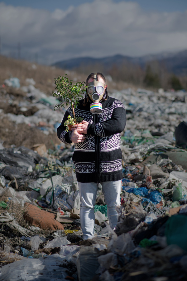 Man with gas mask and potted plant on landfill, environmental concept.