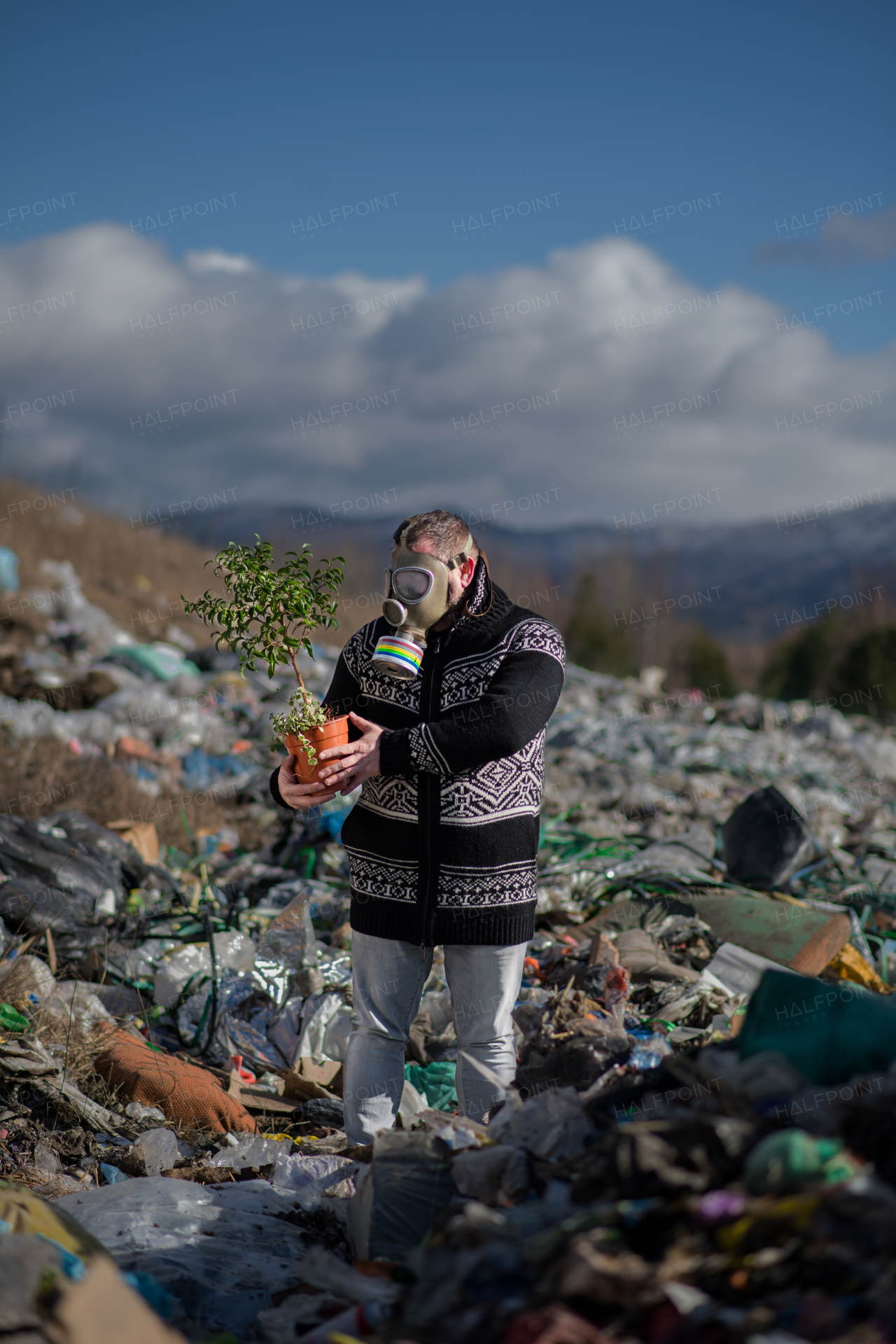 Man with gas mask and potted plant on landfill, environmental concept.