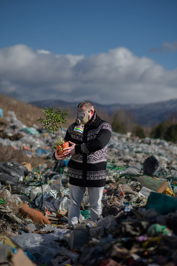 Man with gas mask and potted plant on landfill, environmental concept.