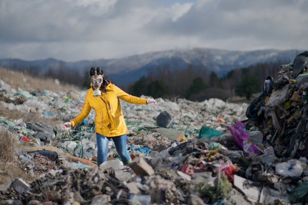 Woman with gas mask walking on landfill, environmental concept. Copy space.