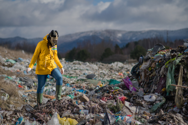 Woman with gas mask walking on landfill, environmental concept. Copy space.