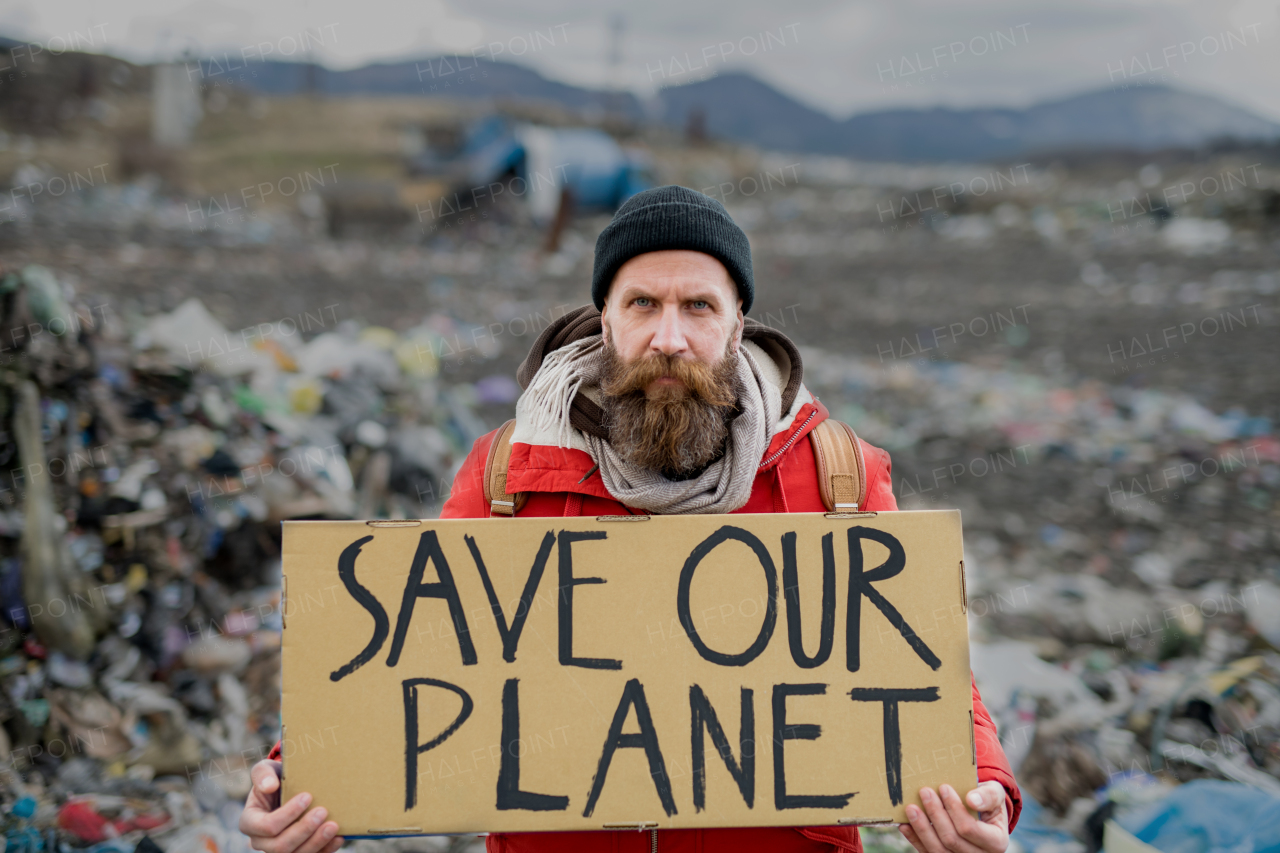 Mature hipster man holding placard poster on landfill, environmental pollution concept.