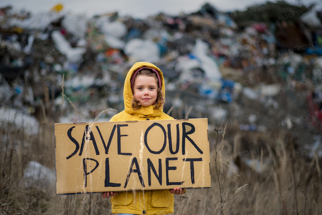 Front view of small child holding placard poster on landfill, environmental pollution concept.