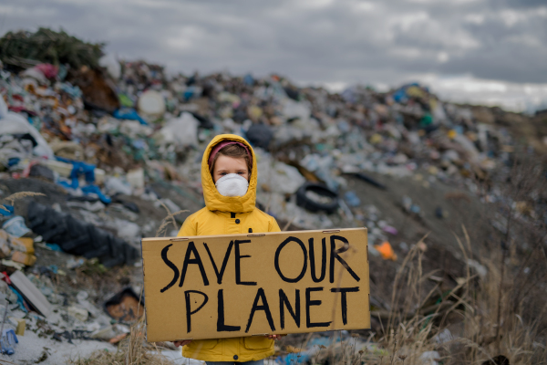 Front view of small child holding placard poster on landfill, environmental pollution concept.