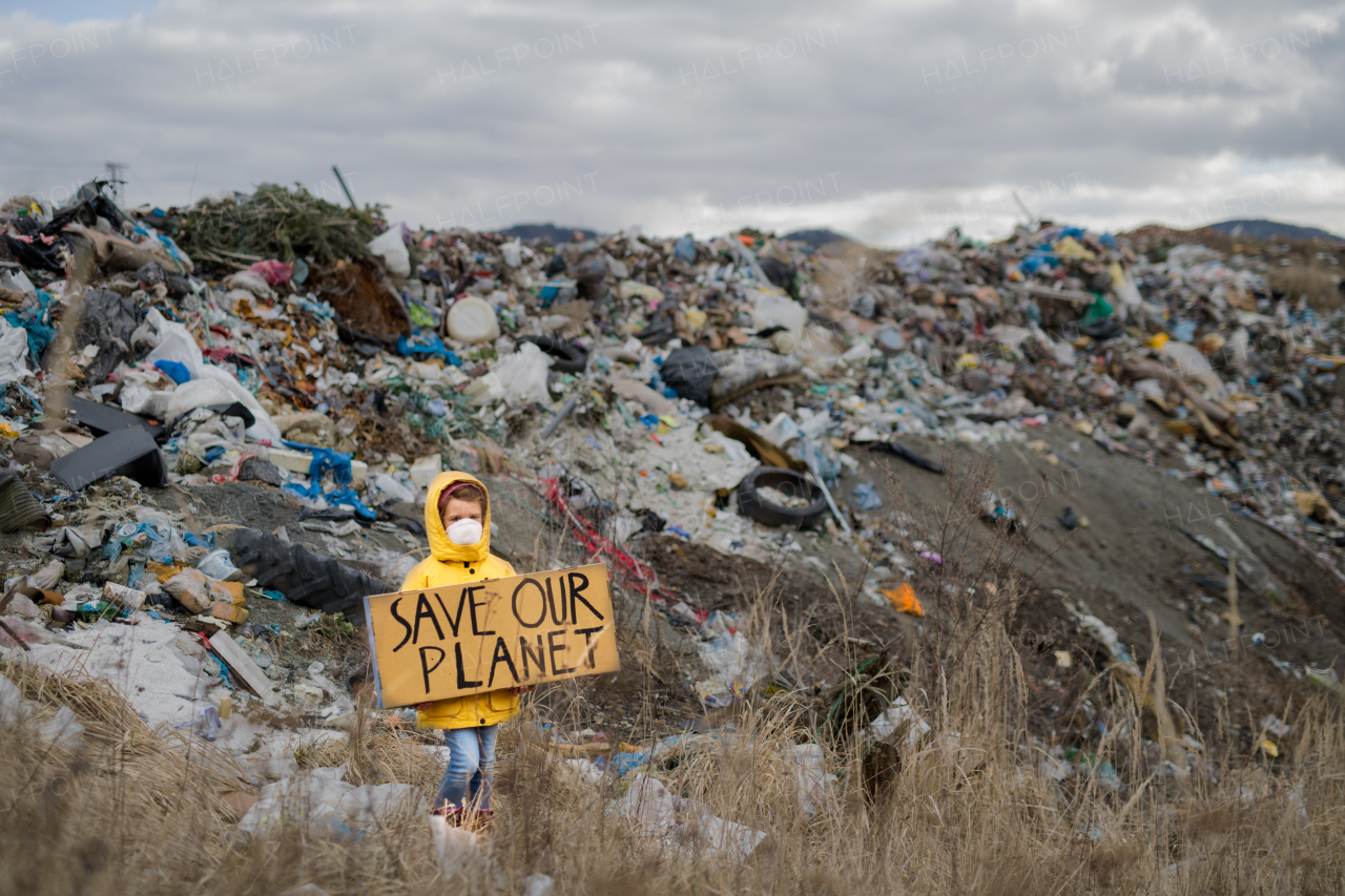 Front view of small child holding placard poster on landfill, environmental pollution concept.