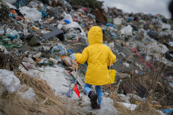 Rear view of small child walking on landfill, environmental pollution concept. Copy space.