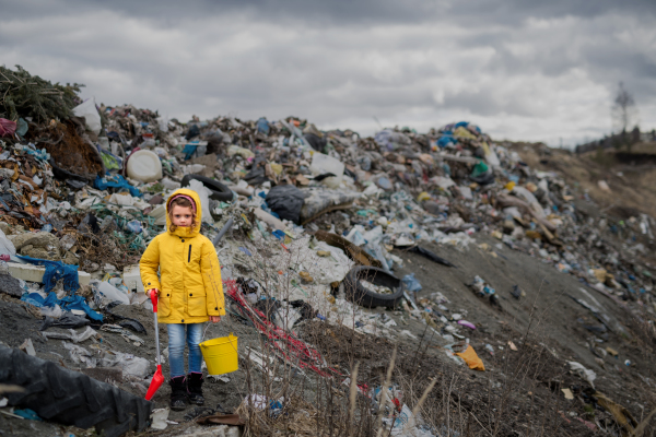 Front view of small child standing on landfill, environmental pollution concept. Copy space.