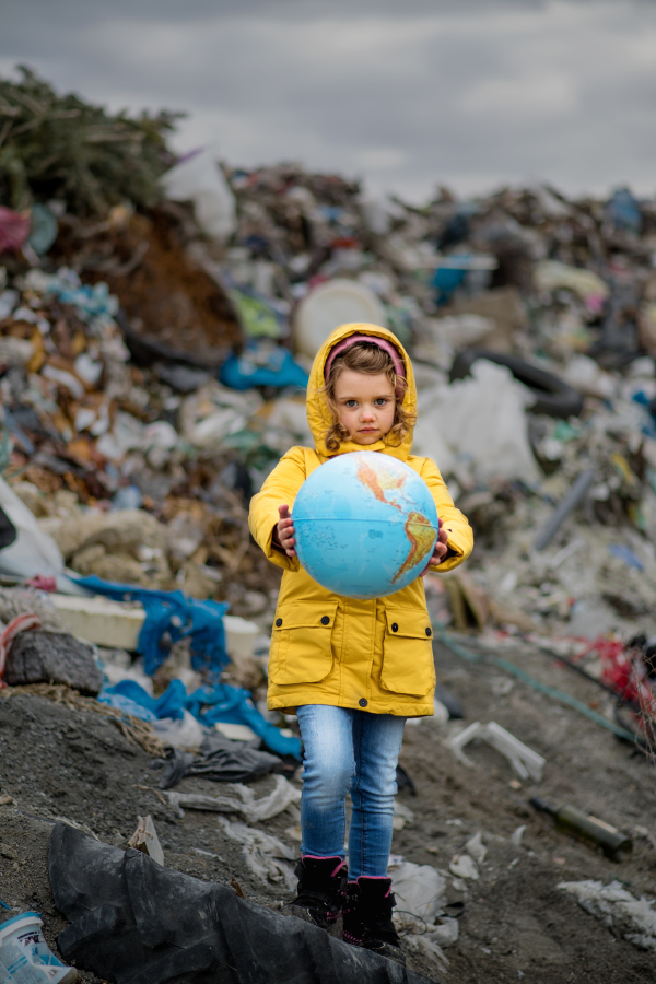 Front view of small child holding globe on landfill, environmental pollution concept.