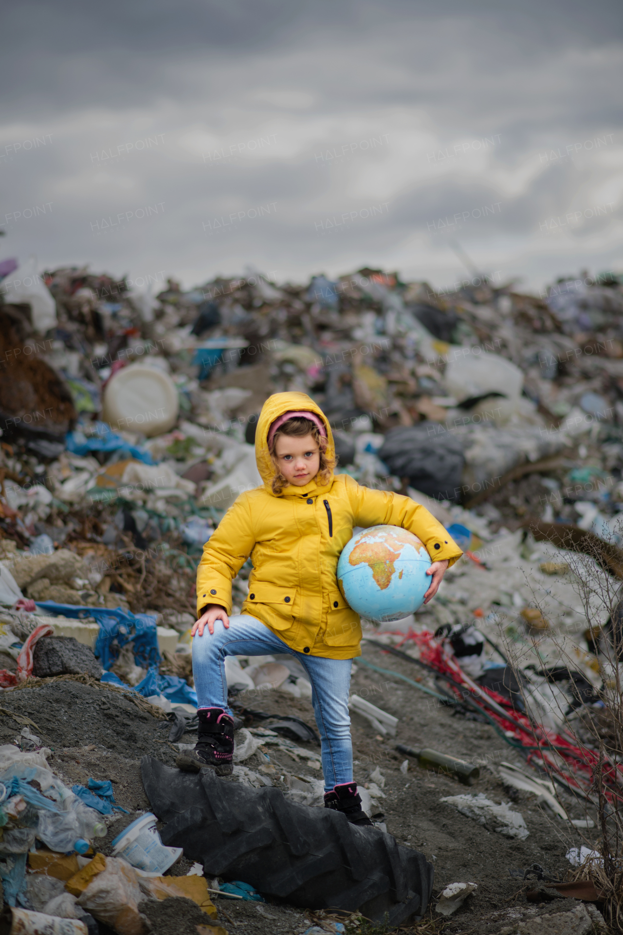 Front view of small child holding globe on landfill, environmental pollution concept.