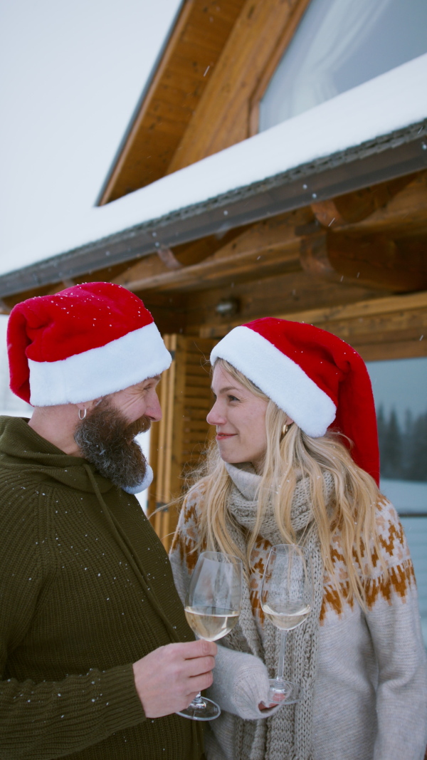 Vertical footage of couple in santa hat with wine glasses outdoors in winter nature, holiday at Christmas time