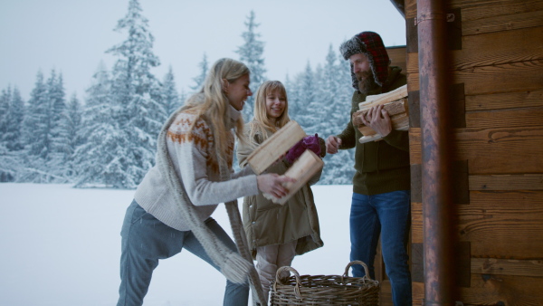 A family with small daughter taking firewood outdoors on terrace , holiday in winter nature.