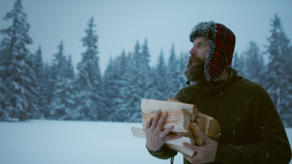 A mature man carrying firewood outdoors in snowy winter nature.