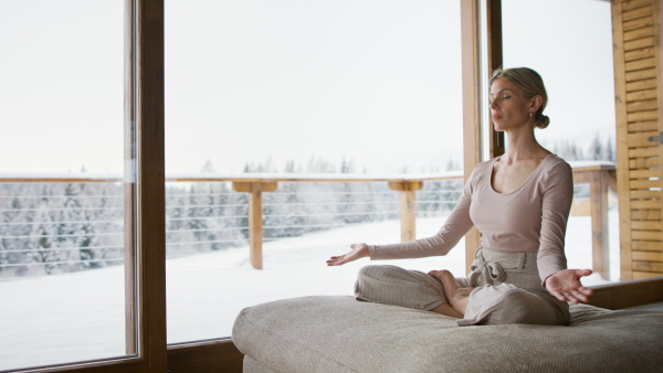 A mid adult woman sitting and exercising yoga indoors in winter apartment.