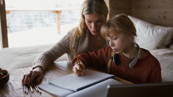 A mother with small daughter doing homework indoors at home, home scholl concept.