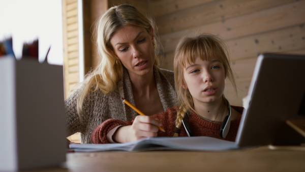 A mother with small daughter doing homework indoors at home, home scholl concept.