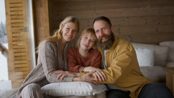 Happy family with small daughter embracing, and looking at camera indoors, winter holiday in private apartment.