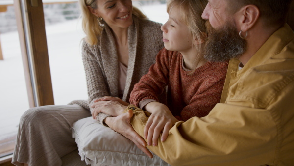 A family with small daughter sitting on sofa and hugging indoors, winter holiday in private apartment.