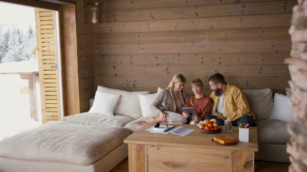 A family with small daughter embracing, and looking at tablet indoors, winter holiday in private apartment.