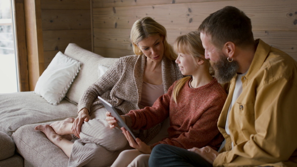 A family with small daughter embracing, and looking at tablet indoors, winter holiday in private apartment.