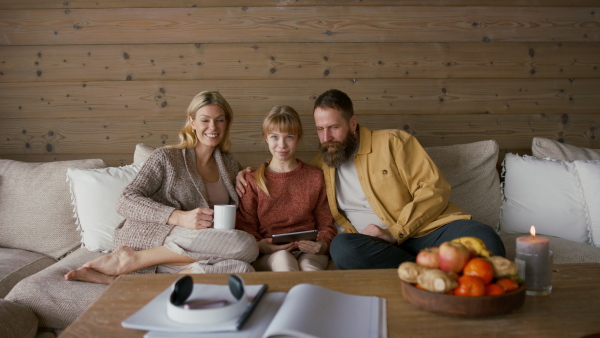 A family with small daughter sitting on sofa and looking camera indoors, winter holiday in private apartment.