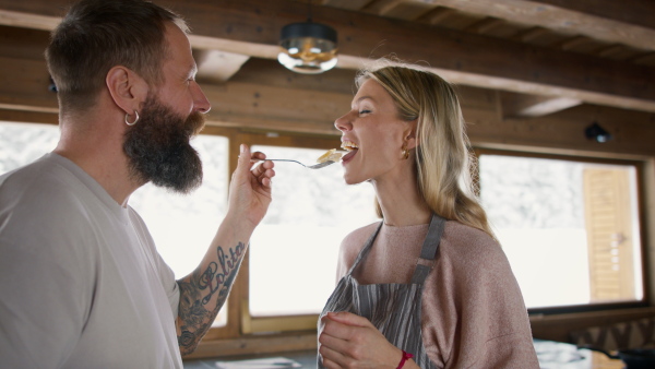 A happy mature couple in love cooking and eating together indoors, winter holiday in private apartment