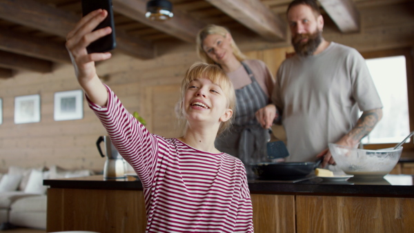 A family with small daughter taking selfie when cooking indoors, winter holiday in private apartment.