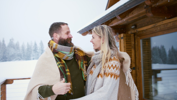 A happy mature couple in love enjoying holiday in mountain hut, standing outdoors and hugging.