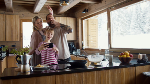 A family with small daughter taking selfie when cooking indoors, winter holiday in private apartment.