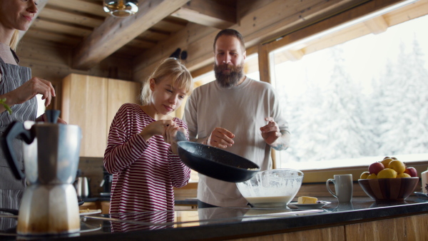 A small girl with parents cooking together indoors, winter holiday in private apartment.