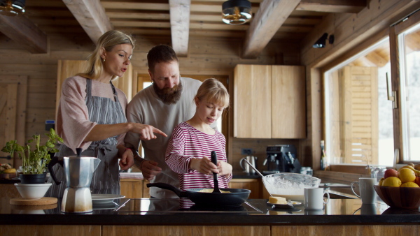 A small girl with parents cooking together indoors, winter holiday in private apartment.