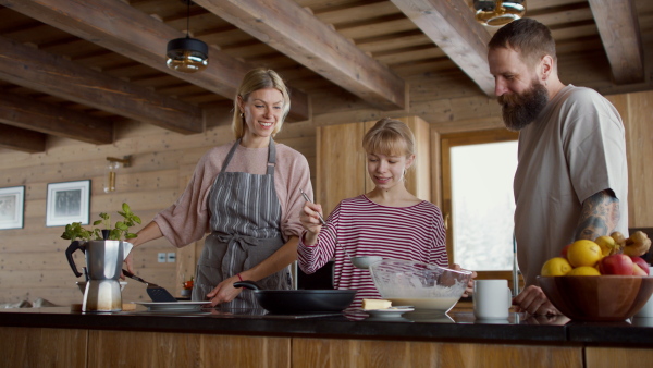 A small girl with parents cooking together indoors, winter holiday in private apartment.