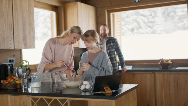 A small girl with parents cooking together indoors, winter holiday in private apartment.