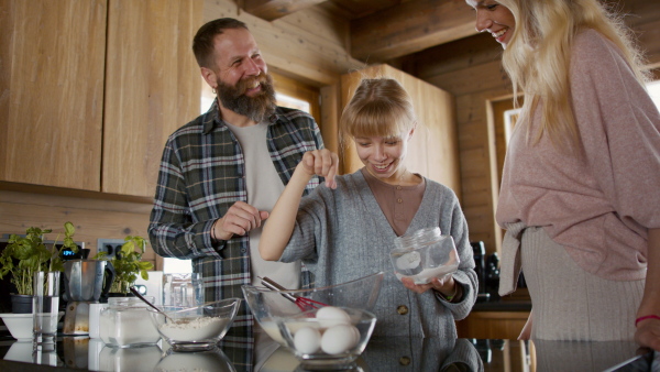 A small girl with parents cooking together indoors, winter holiday in private apartment.