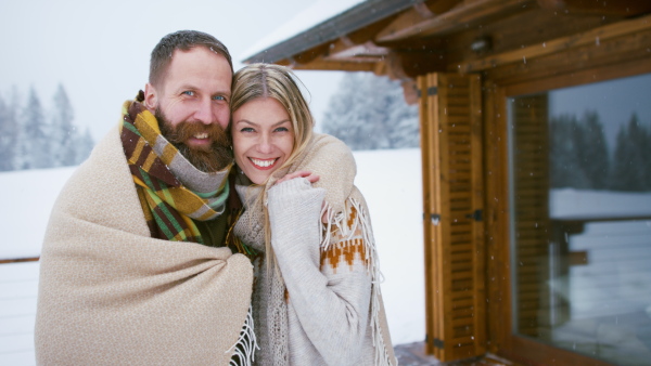 A happy mature couple in love enjoying holiday in mountain hut, standing outdoors and hugging.