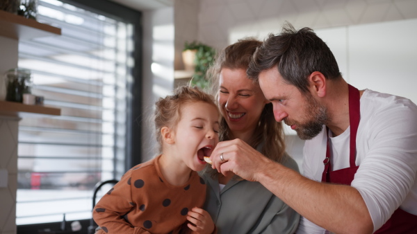 A happy young parents with little daughter in kitchen preparing food and tasting together at home.