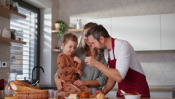 A happy young parents with little daughter in kitchen preparing food and tasting together at home.