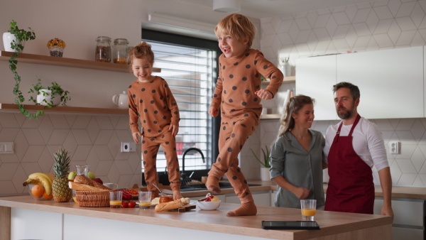 A young family with two little children preparing breakfast together in kitchen and having fun