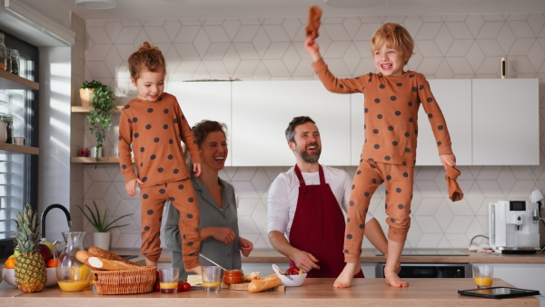 A young family with two little children preparing breakfast together in kitchen and having fun