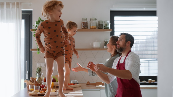 A young family with two little children preparing breakfast together in kitchen and having fun