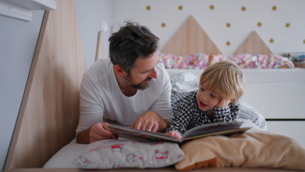 A cheerful father reading book to his little son in bed at home in evening.