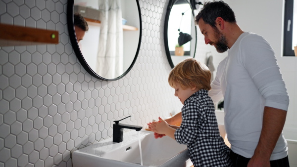 A father with small child indoors in bathroom in the morning at home, washing hands.