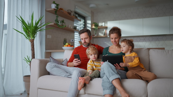 Little children sitting with parents on a sofa and using tablet at home