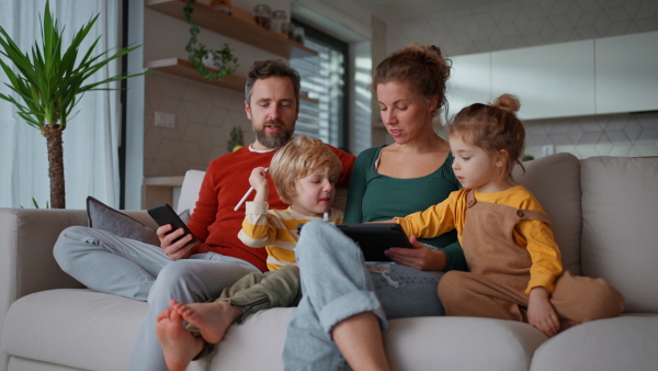 Little children sitting with parents on a sofa and using tablet at home