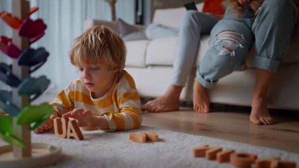 A little boy playing with wodden toys at home, her parents at background