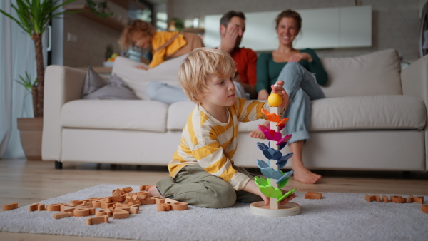 A little boy playing with wodden toys at home, his parents at background